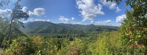 Panoramic view of lush green mountains under a blue sky with fluffy white clouds.