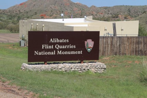 Sign for Alibates Flint Quarries National Monument, with a building and rocky landscape in the background.