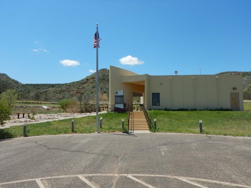 A building with a flagpole in front, surrounded by green grass and hills under a clear blue sky.