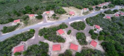 Aerial view of a rural area with small houses, red roofs, and surrounding greenery along a winding road.