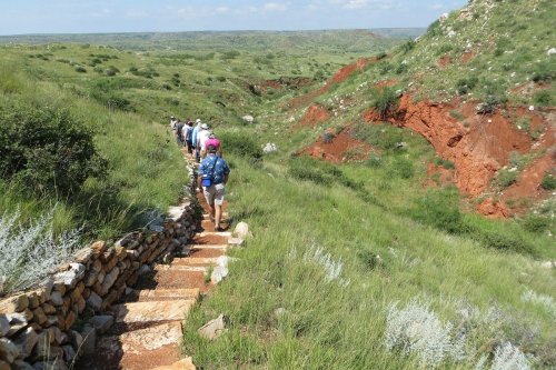 A group of hikers walking along a stone path through a green landscape with red rock formations in the background.