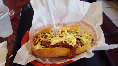 A loaded sandwich with shredded meat, cheese, and toppings, served in a basket with a fork on top.