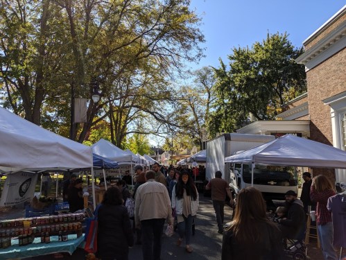 A bustling outdoor market with white tents, vendors, and crowds of people enjoying the autumn day.