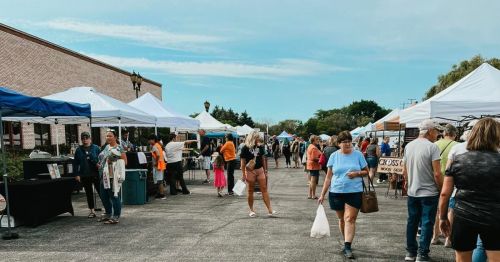 A bustling outdoor market with people browsing vendor tents under a clear blue sky.