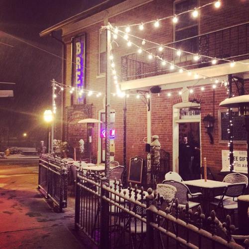 A cozy restaurant exterior at night, adorned with string lights and snow gently falling on the tables and chairs.