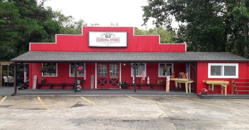 A red general store with a sign reading "Route 62 General Store," featuring a porch and decorative items outside.