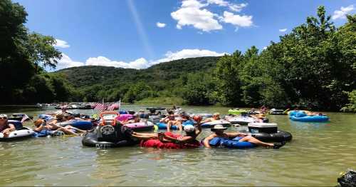 A group of people floating on inner tubes in a river, surrounded by lush greenery and blue skies.