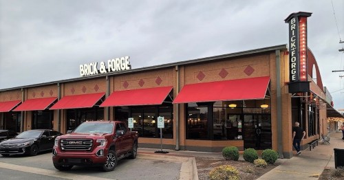 Exterior of Brick & Forge restaurant with red awnings, a GMC truck parked outside, and a cloudy sky above.