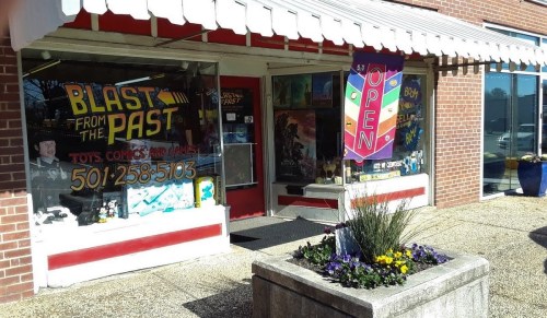 A storefront with a sign reading "Blast from the Past," featuring toys, comics, and games, with an "Open" banner.