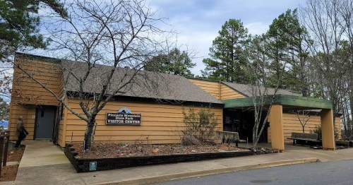 A visitor center building surrounded by trees, featuring a sign that reads "Pinnacle Mountain State Park Visitor Center."