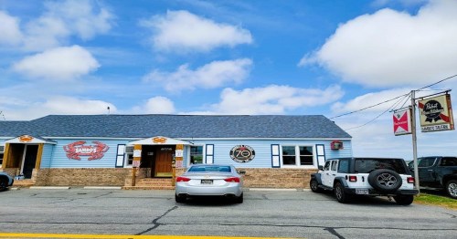 A blue building with a sign for a restaurant, featuring parked cars and a clear sky in the background.