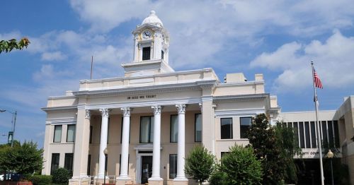 Historic courthouse with a clock tower, columns, and an American flag, set against a blue sky with clouds.