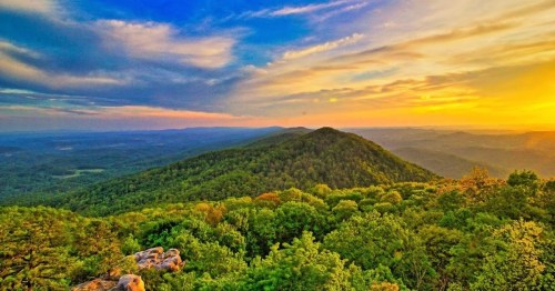 A scenic view of rolling green hills under a colorful sunset sky, with clouds scattered across the horizon.