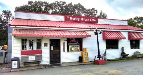 A quaint cafe with a red roof and awnings, featuring a sign that reads "The Hurley House Cafe" and an open sign in the window.
