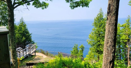 Scenic view of a calm blue lake surrounded by trees, with a wooden path leading to the water's edge.