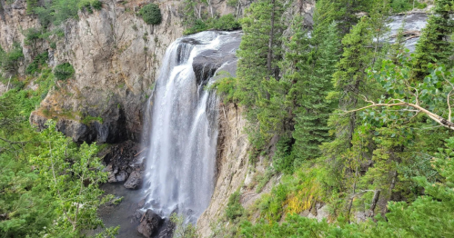 A cascading waterfall flows down rocky cliffs, surrounded by lush green trees and vegetation.