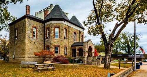Historic stone building with a tower, surrounded by trees and autumn foliage, in a small town setting.