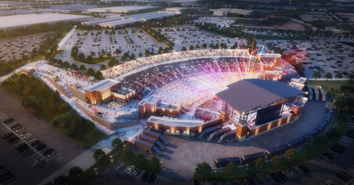 Aerial view of a modern stadium with a large crowd, vibrant lights, and surrounding parking lots.