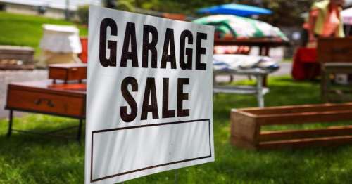 A sign reading "Garage Sale" in front of various items for sale on a sunny day.