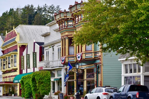 Colorful historic buildings line a street, featuring ornate architecture and greenery in a charming town setting.