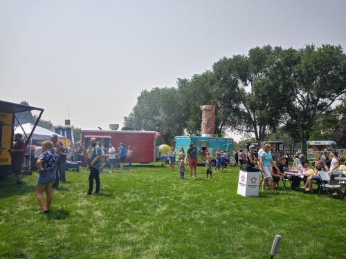 A lively outdoor food truck event with people enjoying food and activities on a sunny day in a grassy area.