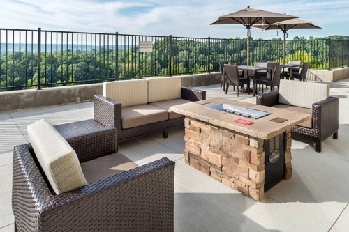 Outdoor seating area with wicker furniture and a stone fire pit, overlooking a scenic landscape under a blue sky.