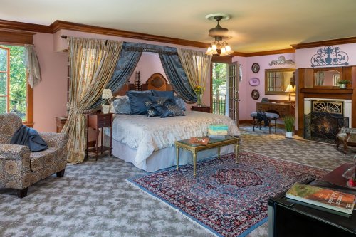 Cozy bedroom with a large bed, elegant curtains, a fireplace, and a vintage armchair, featuring warm colors and decor.