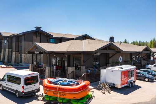 A lodge with a wooden exterior, featuring a large entrance, parked vehicles, and a colorful raft in front.