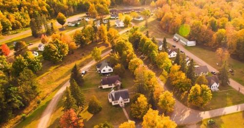Aerial view of a neighborhood surrounded by vibrant autumn trees and winding roads.