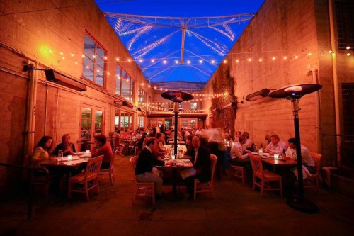 A cozy outdoor restaurant with string lights, diners at tables, and a clear blue sky above.