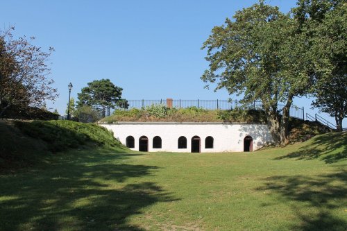A historic stone building with arched windows, surrounded by grass and trees, under a clear blue sky.