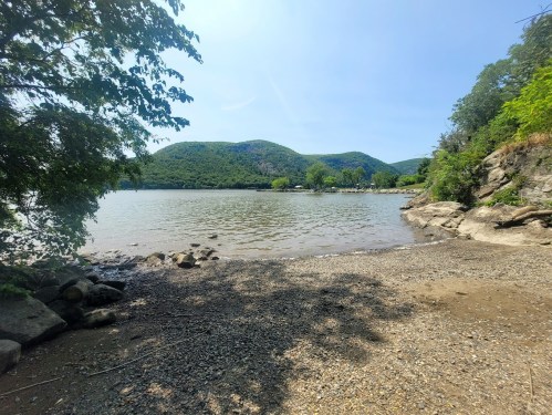A serene lakeside view with rocky shorelines, green hills, and clear blue skies.