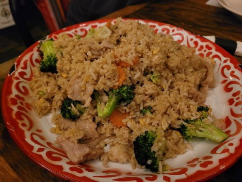 A colorful plate of fried rice with broccoli, carrots, and pieces of meat, served on a decorative red and white dish.