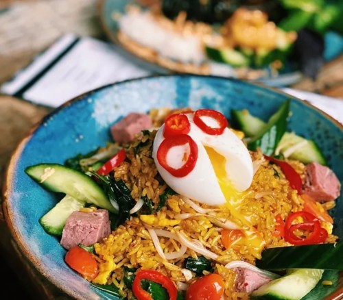 A vibrant bowl of fried rice topped with a poached egg, sliced chili, cucumber, and greens.