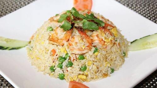 A plate of shrimp fried rice garnished with cilantro, peas, and slices of tomato and cucumber.