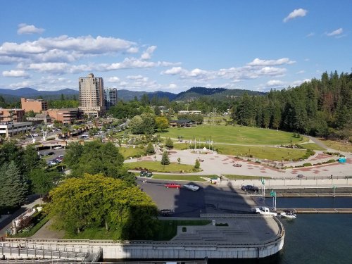 Aerial view of a park with green spaces, trees, and buildings in the background under a blue sky with clouds.