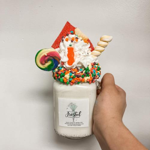 A colorful milkshake topped with whipped cream, sprinkles, candy, and a decorative straw, served in a mason jar.