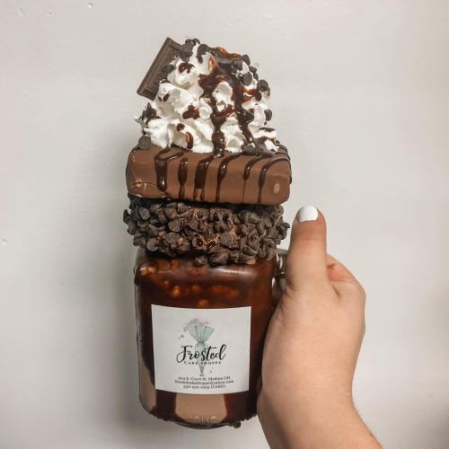 A hand holding a large mason jar filled with chocolate drink, topped with whipped cream, chocolate drizzle, and a candy bar.