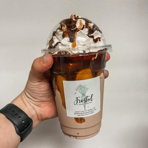 A hand holding a large dessert drink topped with whipped cream, chocolate drizzle, and caramel in a clear cup.