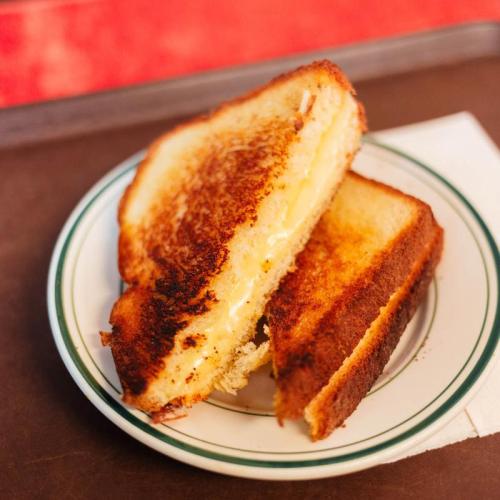 A golden-brown grilled cheese sandwich, cut in half, served on a small plate with a napkin.