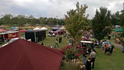 A bustling outdoor festival with food trucks, tents, and crowds enjoying the event in a park setting.