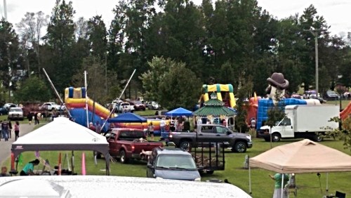 A lively outdoor event featuring inflatable attractions, tents, and people enjoying the festivities in a park.