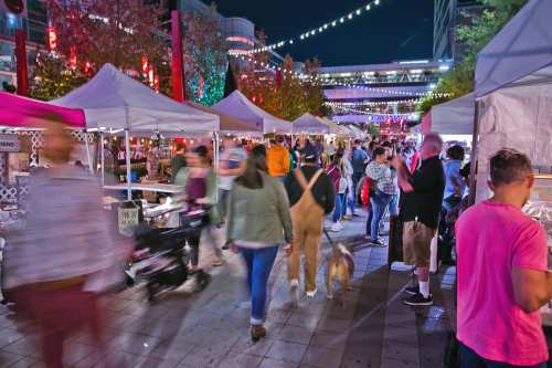 A bustling night market scene with people walking, food stalls, and colorful lights in the background.