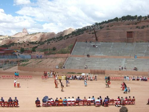 A cultural performance in a desert amphitheater, with dancers in traditional attire and an audience seated in rows.