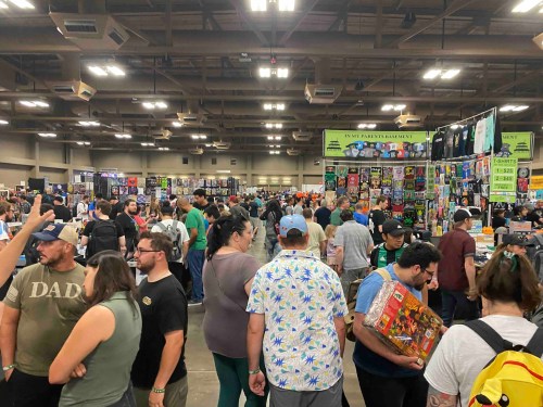 A crowded convention hall filled with people browsing various vendor booths and displays.