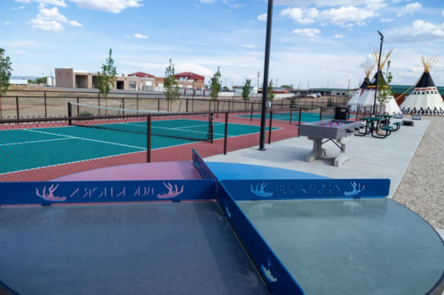 A view of outdoor recreational facilities, including tennis courts and a ping pong table, under a blue sky.