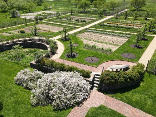 Aerial view of a landscaped garden with pathways, flower beds, and greenery in a sunny outdoor setting.