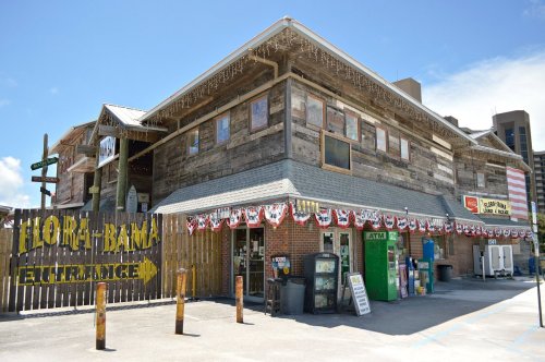 A rustic wooden building with a sign reading "Florabama," decorated with patriotic bunting and an ATM outside.