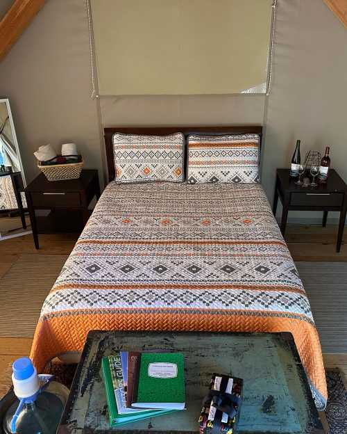 Cozy bedroom with a patterned bedspread, two nightstands, a water bottle, and a notebook on a rustic table.