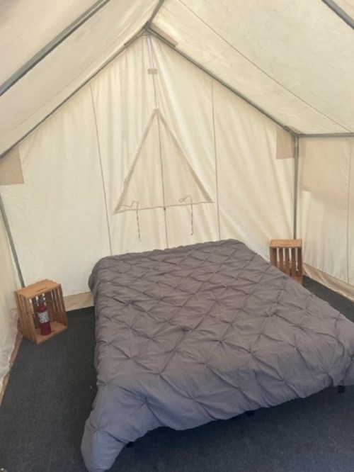A cozy tent interior featuring a bed with a gray comforter and wooden side tables.